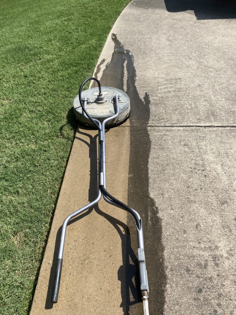 Metal detector resting on a concrete sidewalk next to grass.